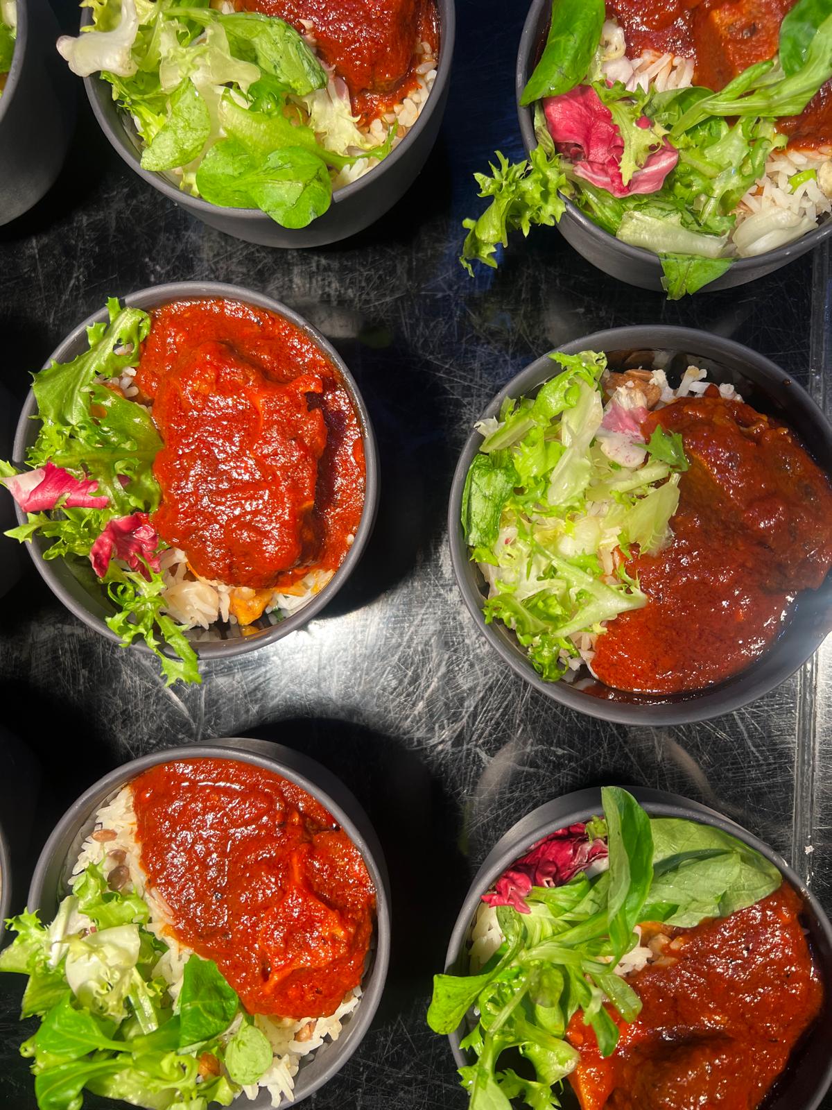 Bowls of rice topped with rich red stew and fresh leaves