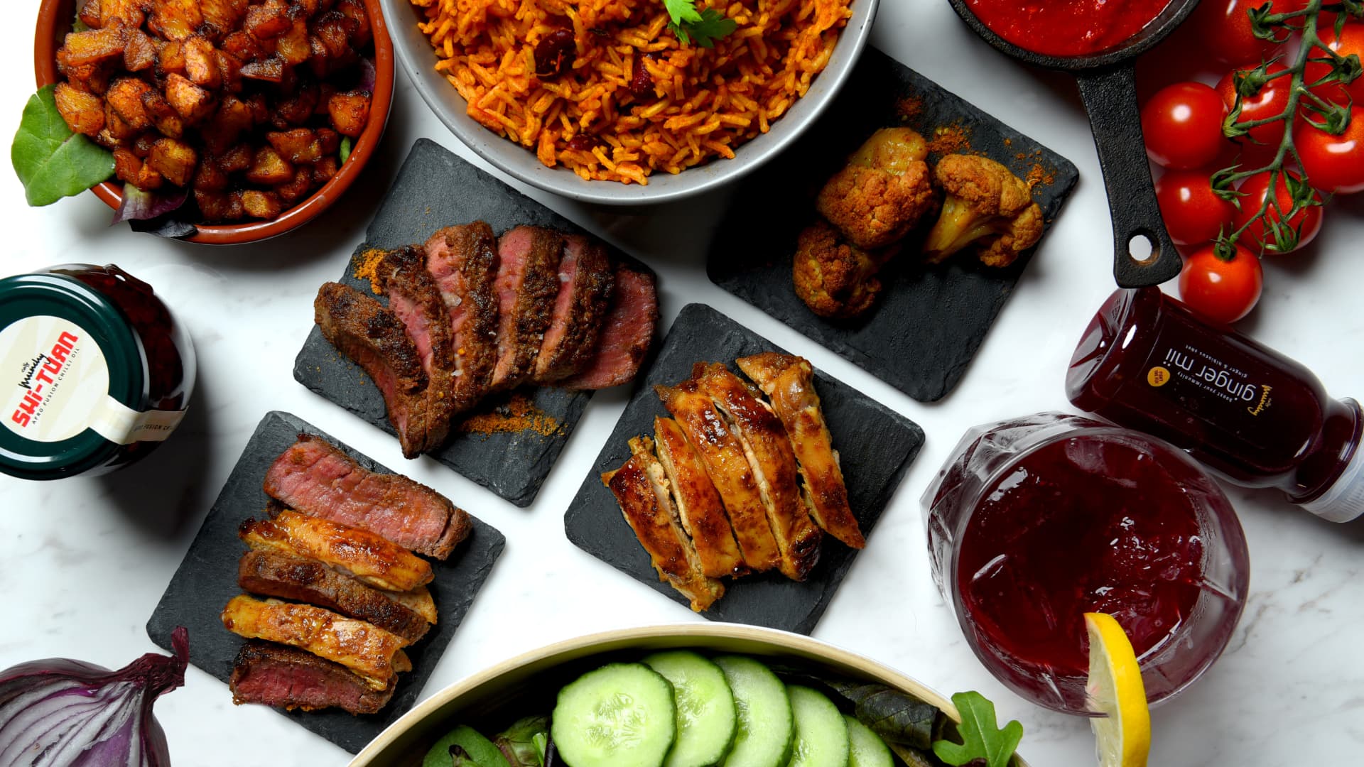 Overhead spread of Cally Munchy dishes, suya steak, jollof and sauces