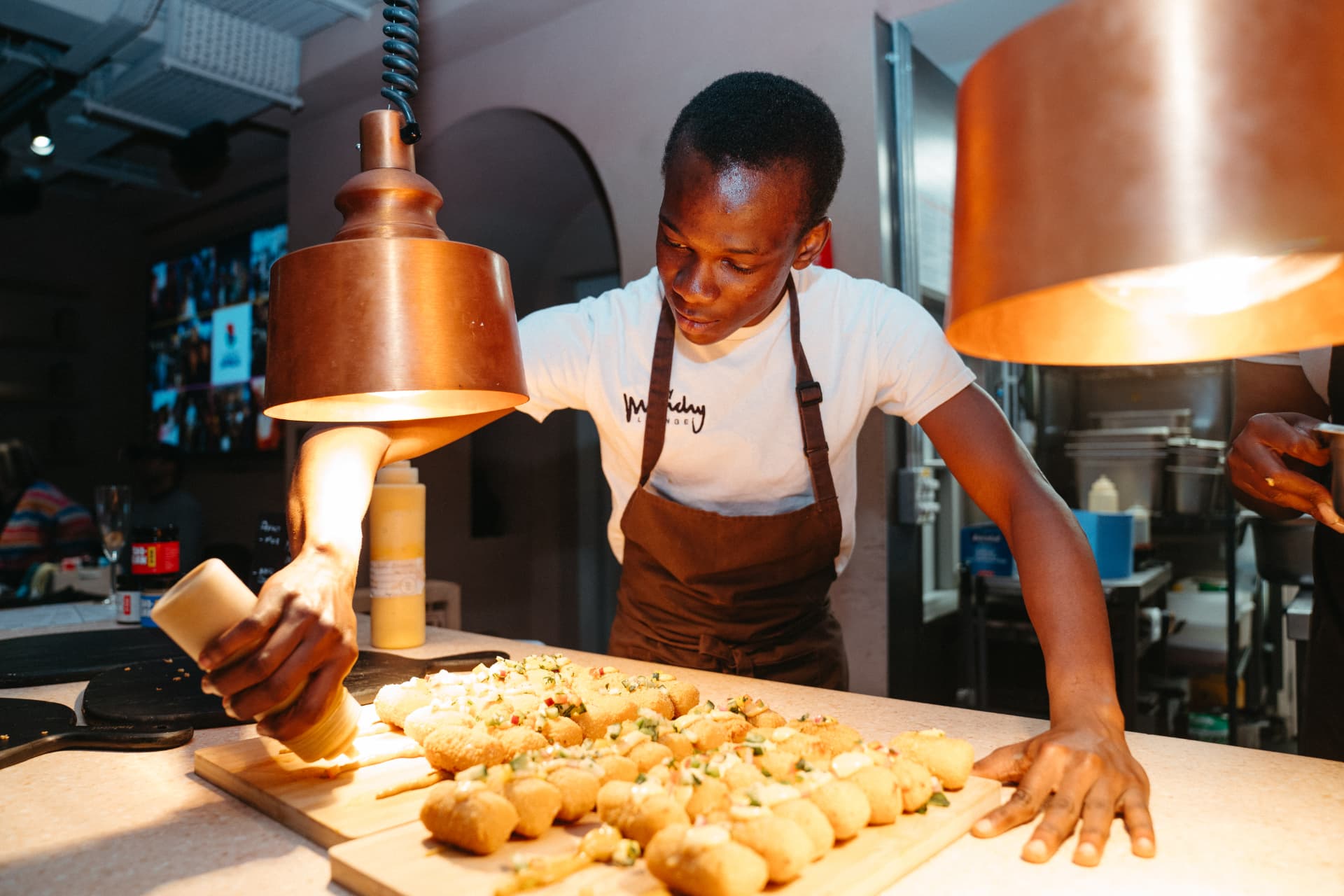 Chef plating fried bites under a copper heat lamp